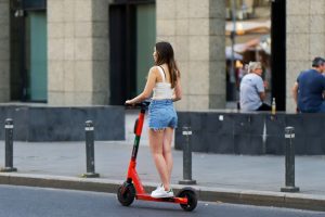 A girl scooting on the street with her scooter. 