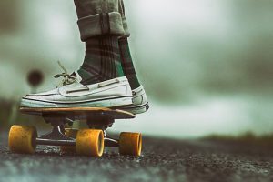 A person wearing a white pair of shoes practices his stunts using his skateboard with yellow wheels. 