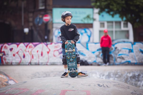 A skateboarding kid in safety gear gripped his skateboard.