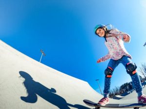 A girl is happily skating at a skatepark, wearing skate gears like knee and elbow pads.