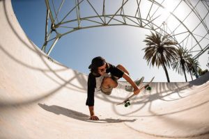 A man wearing a cap doing skateboard trick jumps in the skatepark.