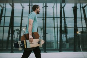 A skateboarder ready for travel with his skateboard.