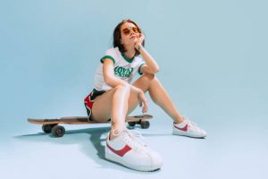 Young woman with glasses sitting on a skateboard, expressing joy with a warm smile.