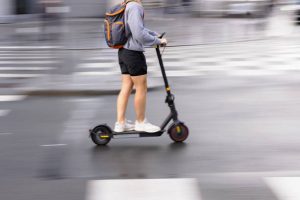 A man trying to ride around the city with a backpack. His scooter has bigger wheels making it a more expensive investment.