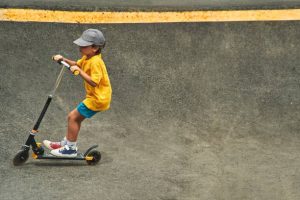 A child is gliding along the ramp on his glide scooter. He is balancing himself well to glide on his scooter.