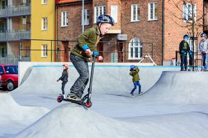 A child is gliding along the ramp on his glide scooter. He is balancing himself to glide on his scooter.