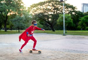 A kid wearing a superman outfit is riding in the park. Skateboard accessory is essential components that enhances skate performance, skate safety, and skate style for riders of all skill levels. From protective gear like helmets, knee pads, and elbow pads to specialized tools for board maintenance and customization, this accessory caters to the diverse needs of skateboard enthusiasts.
