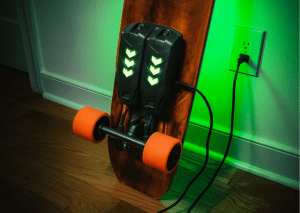 An electric skateboard is placed on the side of the room while being charged. 