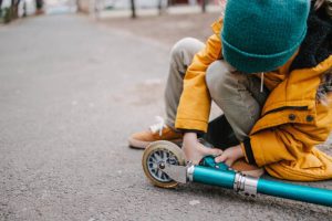 A kid is adjusting his scooter fork. A scooter fork connects the front wheel to the handlebar and allows the rider to steer and control the scooter.