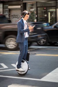 A man wearing headphones is riding a one wheel scooter while listening to his favorite music.