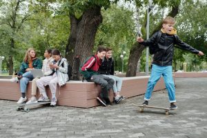 A group of young people gather at the community park; the girls sit and talk while the boys practice their skills. 