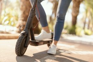 A woman with white shoes rides her adult electric scooter while enjoying the park view on a bright day. 