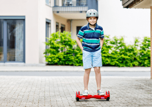 There is a young kid, wearing a helmet. He is dressed in a polo shirt and he is cruising around on a hoverboard. Electric Skateboard and hoverboard