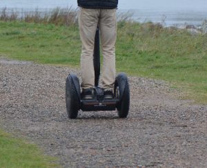 Deck: The image captures the back view of an individual using a self-balancing transporter with a deck, navigating a decked path, showcasing the deck of the device prominently against a natural deck-like backdrop.