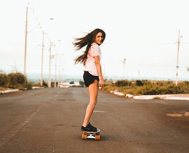 A woman wearing black shorts rides her skateboard while the wind blows her hair. It is nice to use an electric skateboard because of the convenience. 