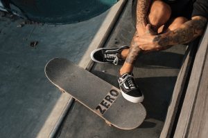 Tattooed individual resting beside a custom 'Zero' skateboard.