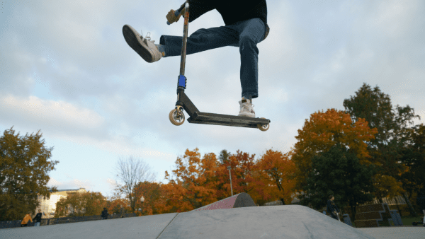 A person does scooter tricks at a skate park. 