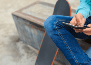 A person sitting with his skateboard while holding his phone. 