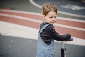 A kid is looking at something while holding her scooter. 