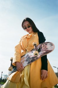 A woman holds her skateboard with gear for skateboarding.