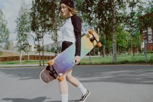 A woman wearing a top brand of skateboarding gear and carries her skateboard.