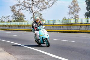 A man with a helmet and a black jacket rides his scooter cautiously.