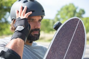 Skateboarding Benefits: A skateboarder takes a moment to rest, holding his skateboard and wearing safety gear, showcasing the importance of protection while enjoying the skateboarding benefits.