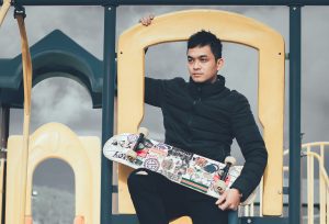 A man wearing a black jacket holding a skateboard 