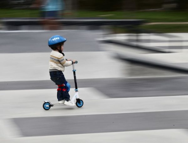 A helmet-wearing child riding a scooter