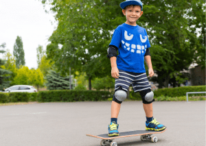 A little boy in blue shirt with blue hat with complete skateboarding gear. Wearing protective equipment while skateboarding is essential to stay safe.