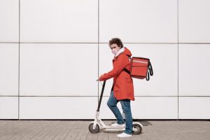 A man with a red bag rides a scooter.