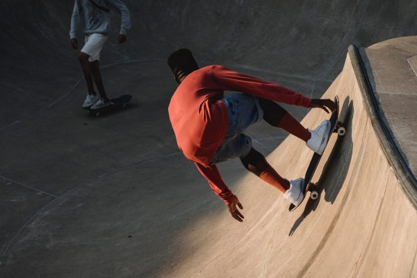 A man with a red-orange sweater in skating in a skatepark. 