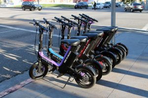 Bunch of scooters lined up outside in the streets.