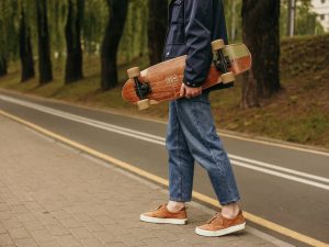 Skateboarder wears fashionable and trendy style of clothing while carrying his board. 