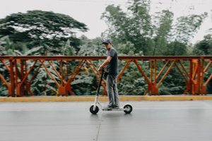 A man with a cap rides his electric scooter, one of the excellent types of scooters available. He's enjoying his type of scooter. 