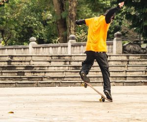 The man in yellow shirt is doing tricks with his skateboard in a public place.