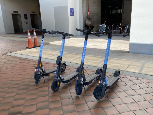 Four scooters with blue color and have new replaced grip tape are parked in a parking lot.