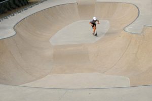 A man is doing stunts for scooters with his scooter at ramps park.