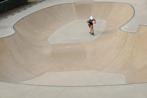 A man is doing stunts with his scooter at scooter park.