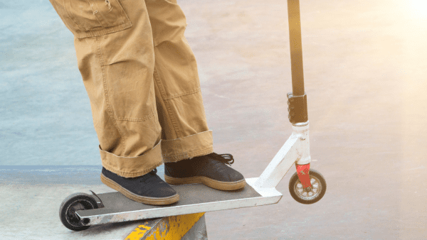 A person wearing brown pants rides his stunt scooter to show his best tricks while maneuvering it. 