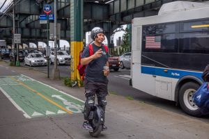 A man with a red bag on his back is riding a black scooter while wearing helmet.