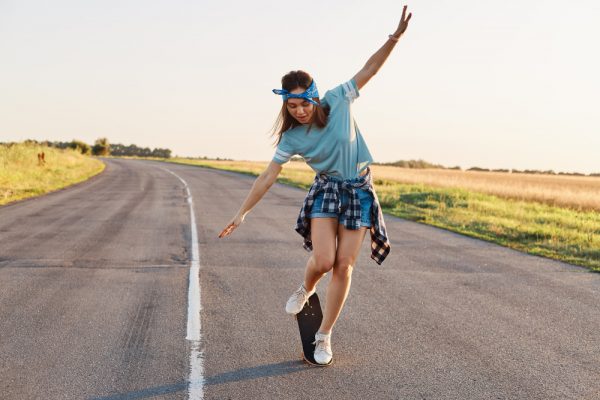 A woman doing tricks in the middle of the road, using the skateboard to relieve stress. 
