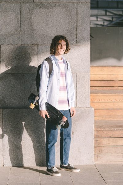 Curly tall man holding his mini black longboard. 