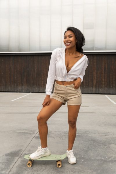 A beautiful girl with white crop top jacket and short is posing with her board. 