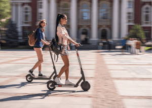 Two women ride scooters