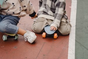 Two kids of toddler age sit on their skateboards for toddler while they talk to each other. 