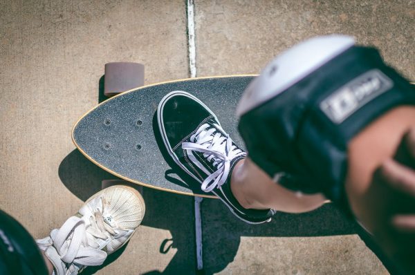 A man wearing his skateboard gear while riding puts his foot on the right skateboard deck for riding.