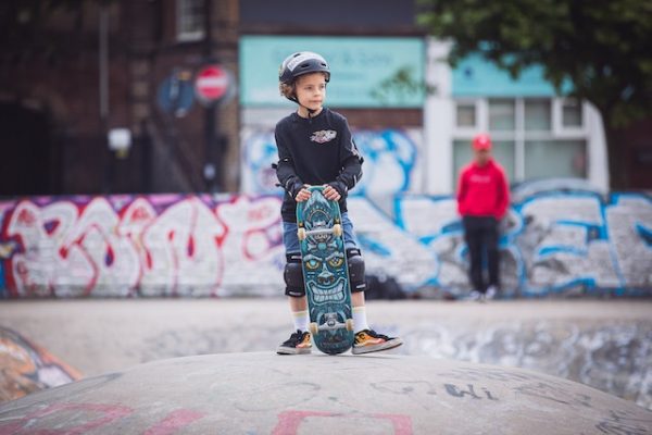A young boy stands on the sidewalk, clutching his longboard with eager anticipation. His eyes sparkle with excitement as he gazes ahead at the perfect spot to unleash his skateboarding skills. The sun casts a warm glow on the pavement, promising an afternoon of thrilling rides. With a determined grin, he imagines the skateboarding twists and skateboarding turns he will conquer, the skateboarding jumps he will master. The sound of skateboarding wheels rolling on concrete fills the air, urging him forward. As he takes a step closer to his chosen longboarding arena, he feels a rush of adrenaline because of longboarding. This kid is having a great day for sure.