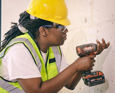 a man is actively engaged in the process of installing scooter wall mounts or bracket. To prioritize safety while installing the wall mount for a scooter, he is wearing appropriate protective gear, which includes safety goggles or eye protectors to shield his eyes from potential hazards, a high-visibility vest for increased visibility and safety, and a yellow hardhat to protect his head. These safety measures indicate a responsible and cautious approach to the task at hand.