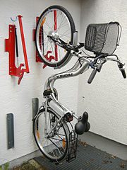 a bicycle is positioned next to a residential structure, likely a house. It appears to be stationary and not in use, as it is parked alongside the building. Surrounding the bicycle, there are several tools placed in close proximity. These tools could serve various purposes, such as maintenance, repairs, or assembly of the bicycle and scooter. The presence of tools suggests that someone might be working on the bicycle or scooter wall mounts, making adjustments, fixing issues, or performing routine maintenance. 